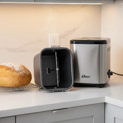 Oster Expressbake Bread Maker with a fresh loaf of bread, showcasing its compact design and easy-to-clean pan.