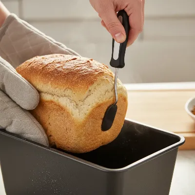 A person carefully removing a loaf of bread from an Elite Gourmet bread maker, illustrating the common issue of a stuck paddle